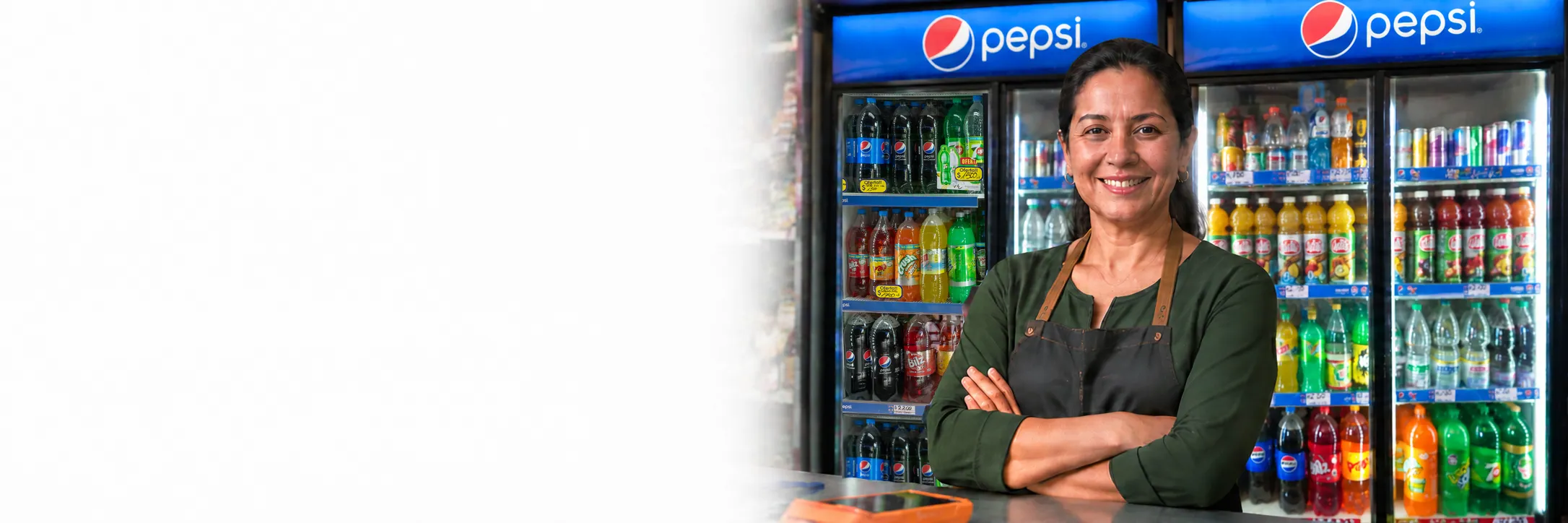 Almacenera sonriente de brazos cruzados frente a los refrigeradores de bebidas de su negocio