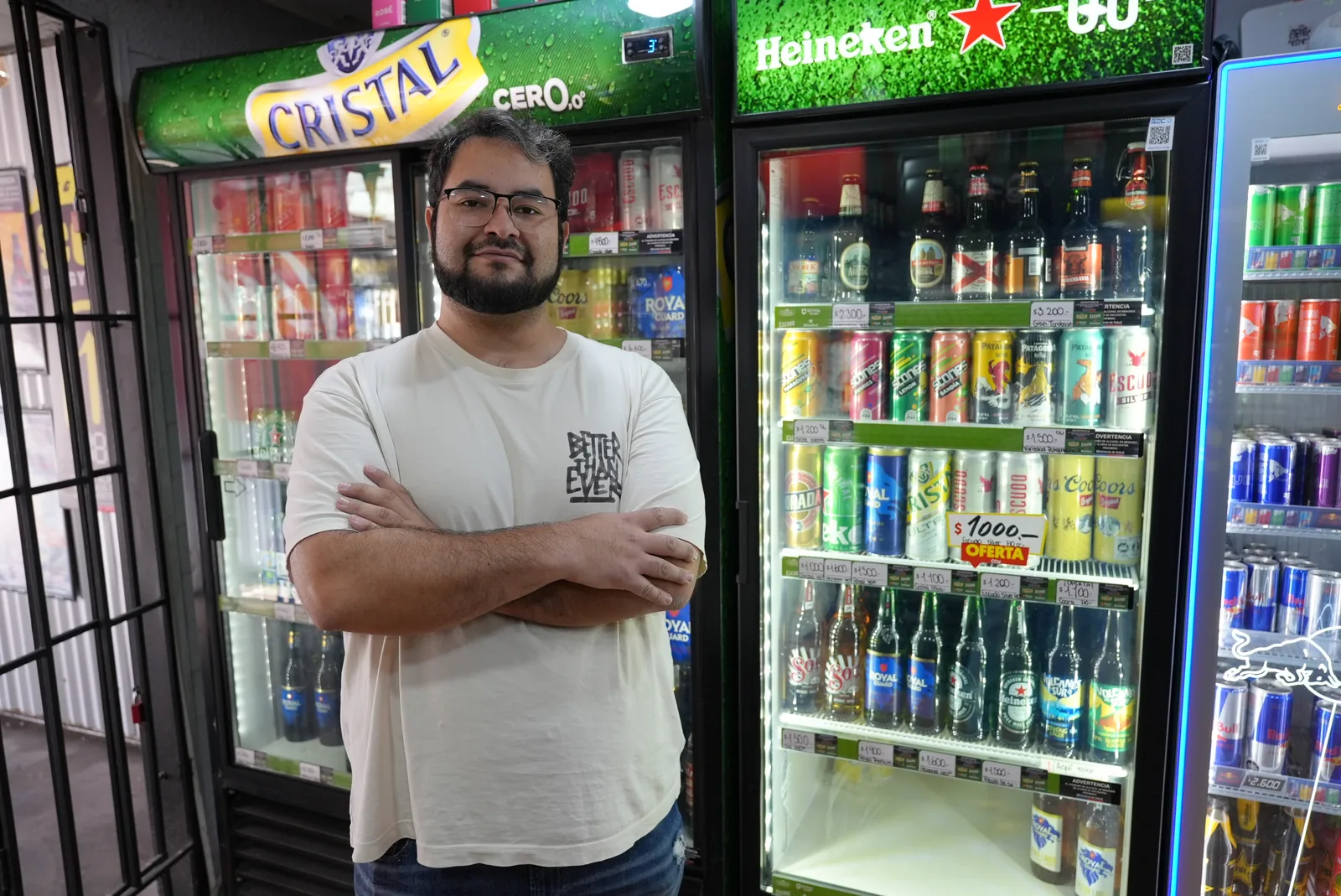 Almacenero de brazos cruzados frente a los refrigeradores de bebidas y cervezas de su local