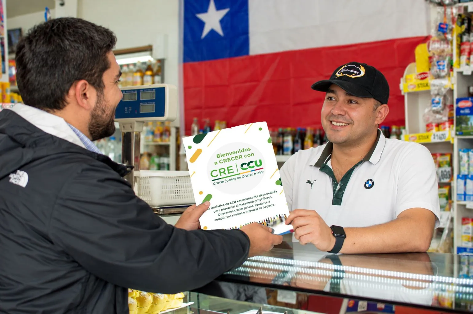 Ejecutivo entrega el folleto de bienvenida de CRECCU a un almacenero en el mesón de su local
