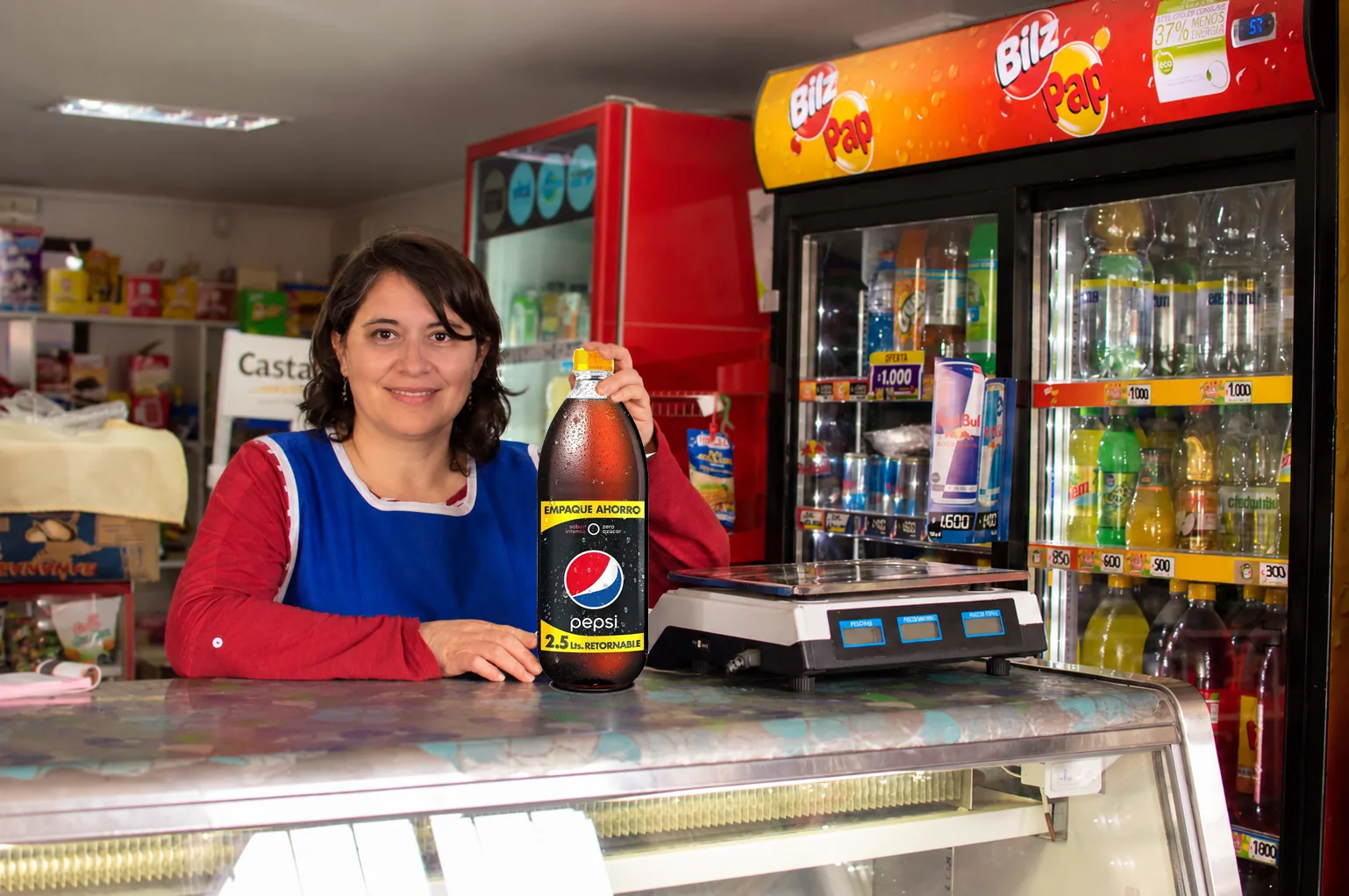 Almacenera sonríe tras el mesón de su local con una botella de Pepsi retornable, junto a una balanza y los refrigeradores de bebidas